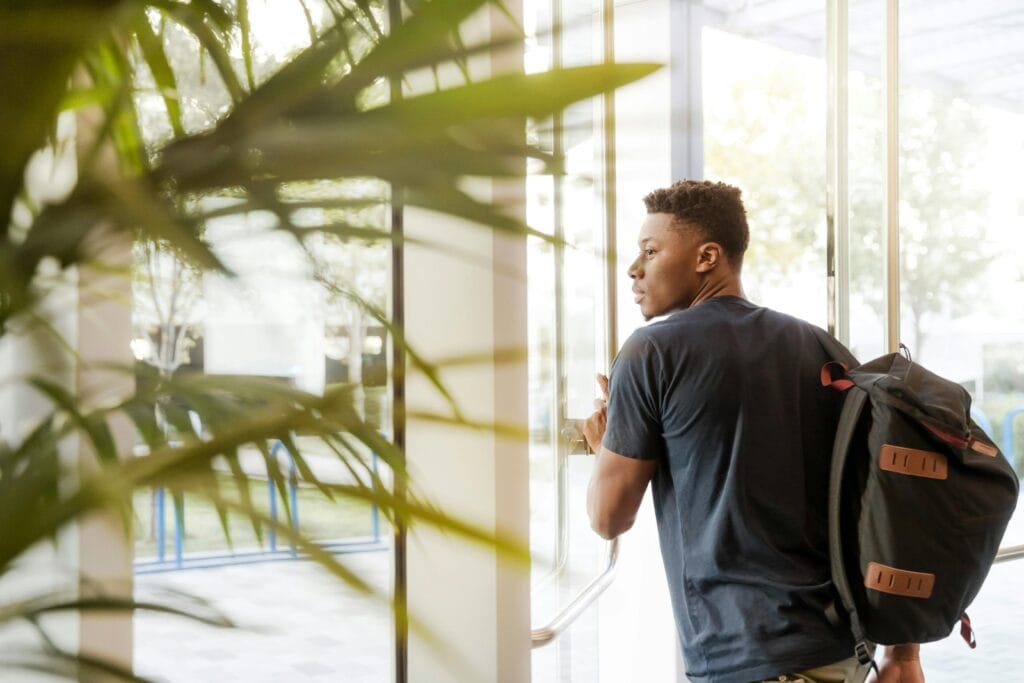 pexels-photo-1251861-1251861 A college student with a backpack exits a campus building through glass doors.