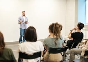 Man presenting with tablet to a small seated audience in a modern indoor setting.