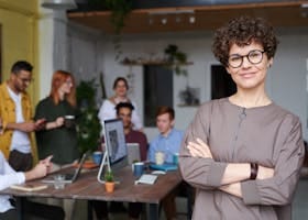 Smiling businesswoman with curly hair stands confidently in a modern office space with colleagues.