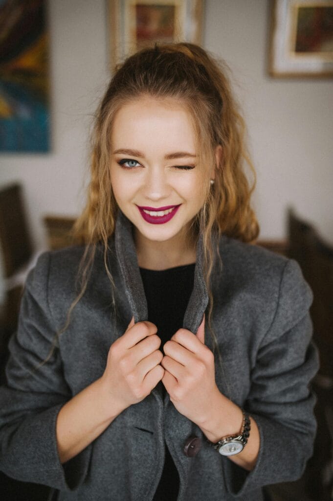pexels-photo-388517-388517 Charming young woman with red lips and casual grey coat winking indoors.
