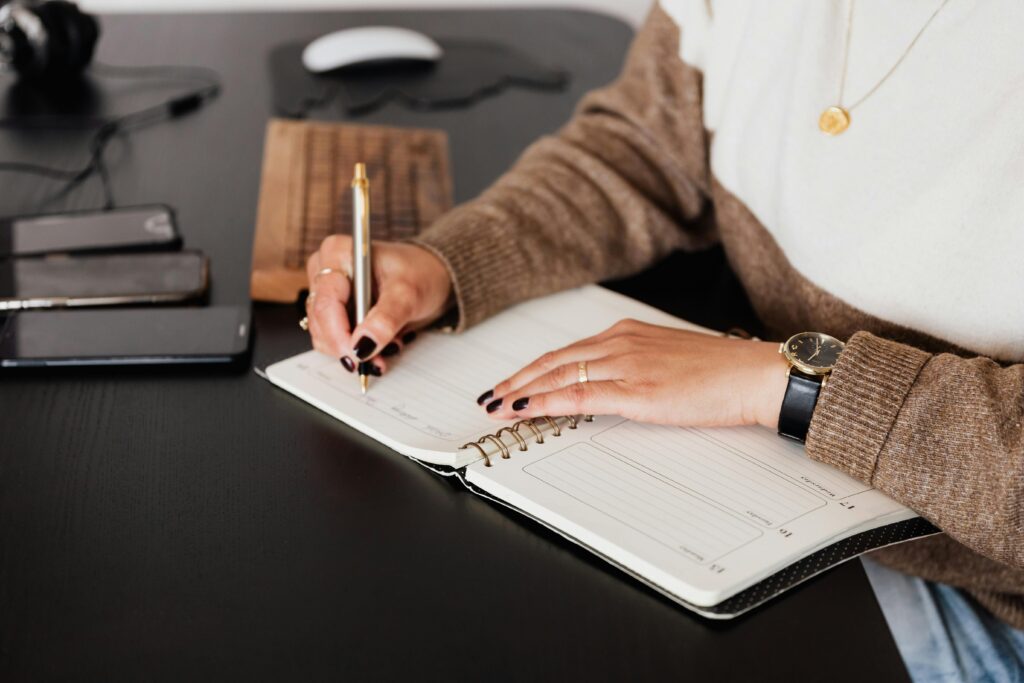 A female freelancer notes plans in a diary at a sleek desk with devices.